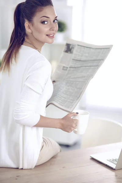 Cute businesswoman holding newspaper sitting at her desk in office