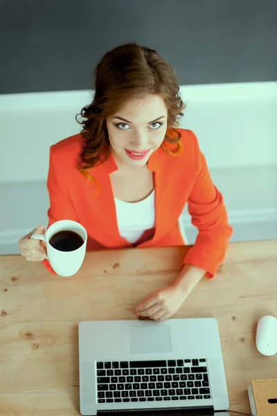 Mulher atraente sentada na mesa no escritório, trabalhando com computador portátil — Fotografia de Stock