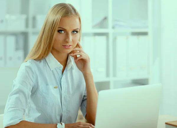 Aantrekkelijke zakenvrouw zit op een bureau met laptop in het kantoor — Stockfoto