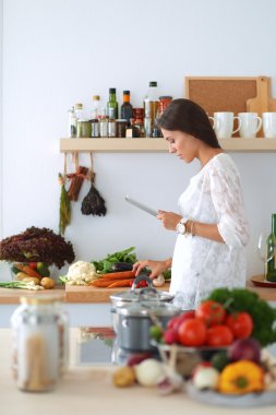 Mutfakta yemek yapmak için tablet bilgisayar kullanan genç bir kadın.