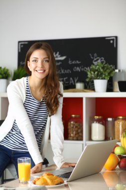 Dizüstü bilgisayar kullanarak ve mutfakta oturmuş çekici genç kadın