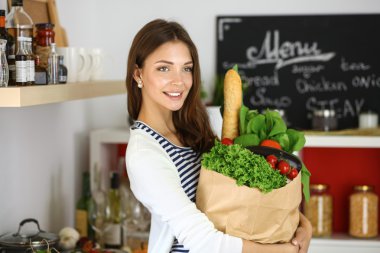 Elinde sebzeli alışveriş torbası tutan genç bir kadın.