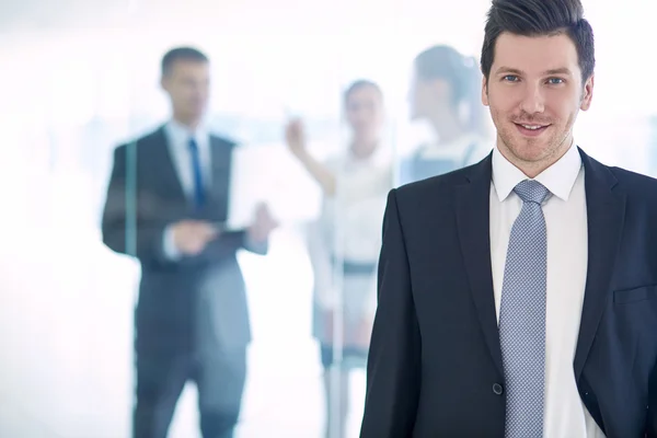 Portret van jonge zakenman in kantoor met collega's op de achtergrond — Stockfoto