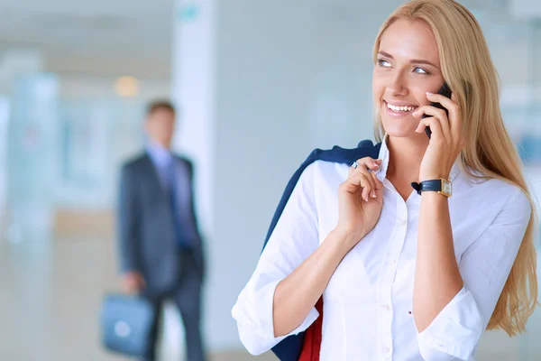 Bizneswoman stoi przy oknie biurowym rozmawiając przez telefon komórkowy — Zdjęcie stockowe