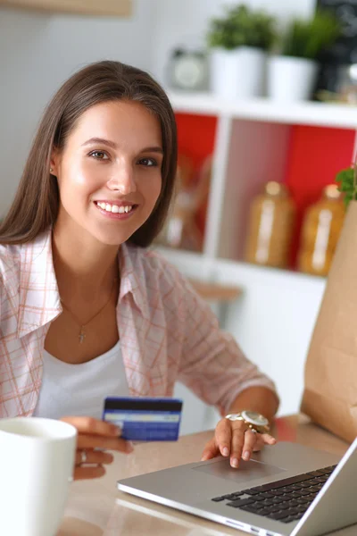 Mulher sorrindo compras on-line usando tablet e cartão de crédito na cozinha — Fotografia de Stock