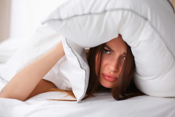 Mujer acostada en la cama y cerrando las orejas con almohada — Foto de Stock