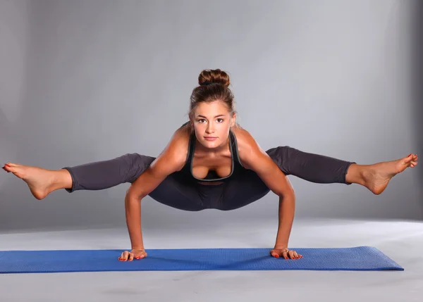 Mladá žena, která dělá jóga cvičení na šedém pozadí — Stock fotografie