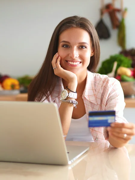 Mulher sorrindo compras on-line usando tablet e cartão de crédito na cozinha — Fotografia de Stock