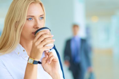 Genç bir iş kadını ofisinde fincanla masada oturuyor.