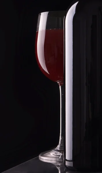 Κομψό ποτήρι κρασί και ένα μπουκάλι κρασί στο μαύρο φόντο. — Φωτογραφία Αρχείου