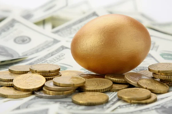 Een gouden ei liggen op dollar en munten. — Stockfoto