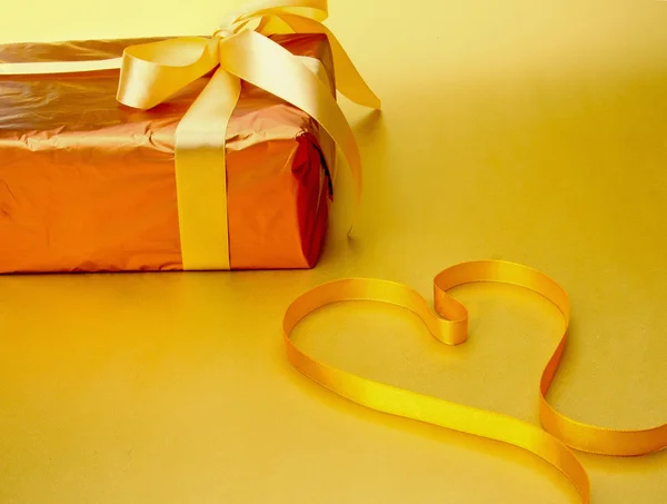 Um presente e uma fita vermelha moldando o coração . — Fotografia de Stock