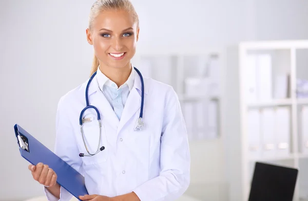 Leende kvinnlig läkare med en mapp i uniform stående på sjukhus Stockbild