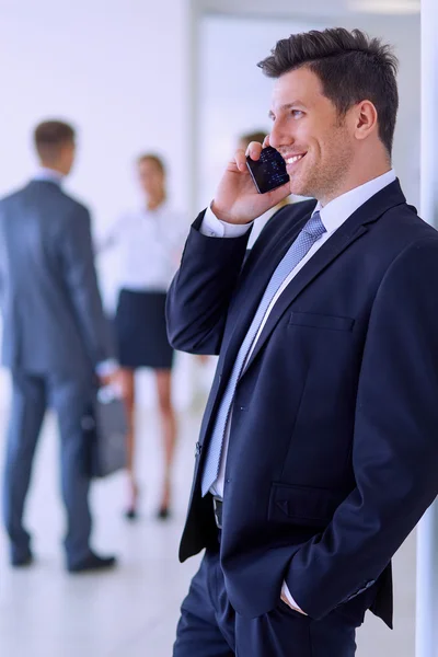 Porträtt av ung affärsman med mobil i office med kollegor i bakgrunden — Stockfoto