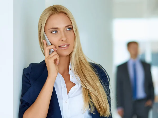 Zakenvrouw staat tegen kantoorraam te praten op mobiele telefoon — Stockfoto