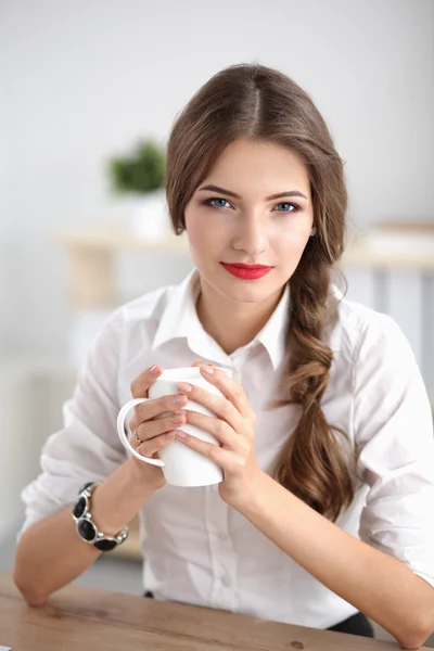 Genç bir iş kadını ofisinde fincanla masada oturuyor. — Stok fotoğraf