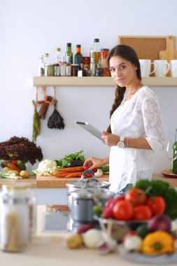 Mutfakta yemek yapmak için tablet bilgisayar kullanan genç bir kadın.