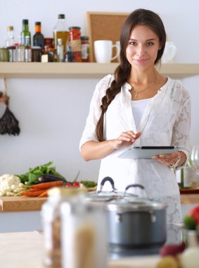 Mutfakta yemek yapmak için tablet bilgisayar kullanan genç bir kadın.