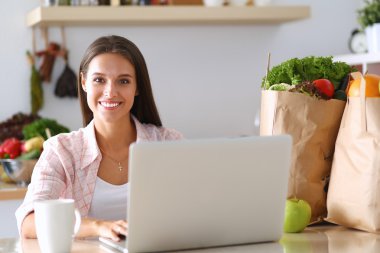 kahve fincanı ve dizüstü evde mutfakta gülümseyen genç kadın