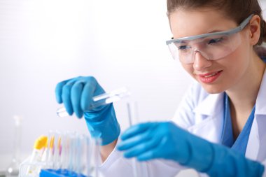 Kadın araştırmacı, beyaz arka planda izole edilmiş ilaç şişeleri ve mataralarla çevrili.