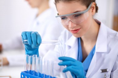 Kadın araştırmacı, beyaz arka planda izole edilmiş ilaç şişeleri ve mataralarla çevrili.