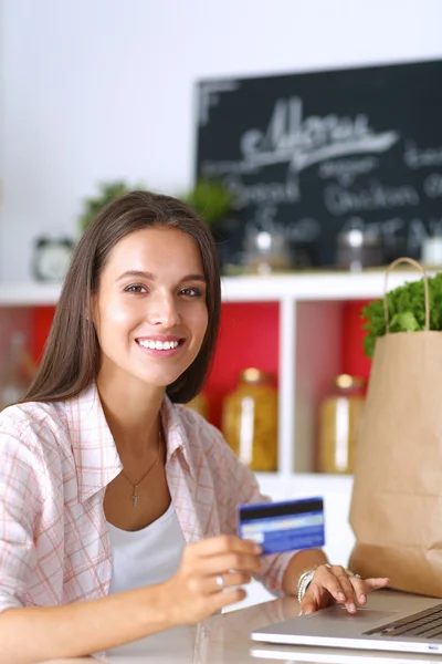 Mulher sorrindo compras on-line usando tablet e cartão de crédito na cozinha — Fotografia de Stock