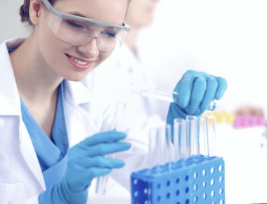 Kadın araştırmacı, beyaz arka planda izole edilmiş ilaç şişeleri ve mataralarla çevrili.