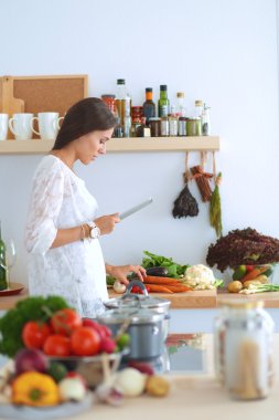 Mutfakta yemek yapmak için tablet bilgisayar kullanan genç bir kadın.