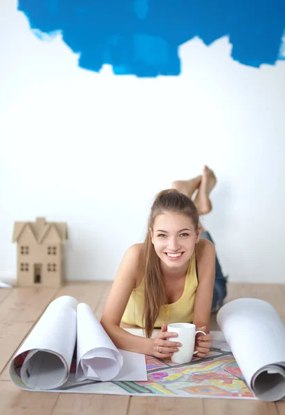 Junge Frau liegt auf dem Boden und betrachtet Bauplan des neuen Hauses — Stockfoto