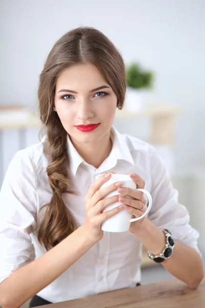 Giovane donna d'affari seduta sulla scrivania con tazza in ufficio — Foto Stock