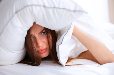 Kadın yatakta uzanıyor ve kulaklarını yastıkla kapatıyor.