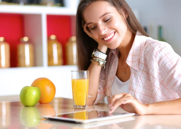 Жінка використовує планшетний комп'ютер під час пиття чаю на кухні — стокове фото
