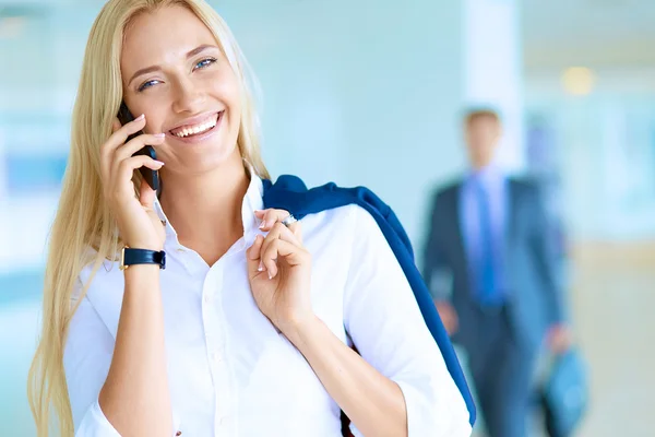 Zakenvrouw staat tegen kantoorraam te praten op mobiele telefoon — Stockfoto