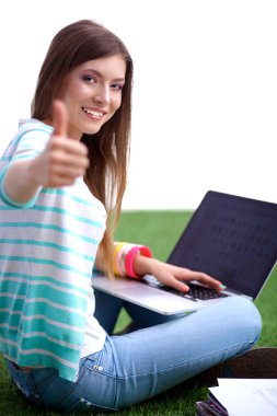 Laptoplu genç bir kadın yeşil çimlerde oturuyor.