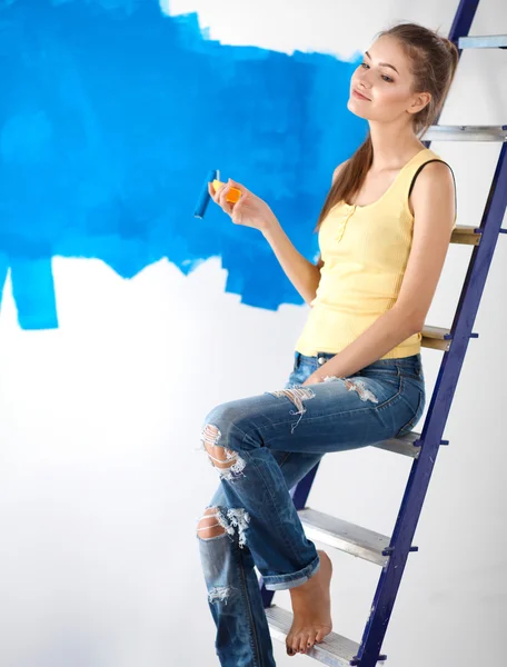 Happy beautiful young woman doing wall painting, standing near ladder — Stock Photo, Image