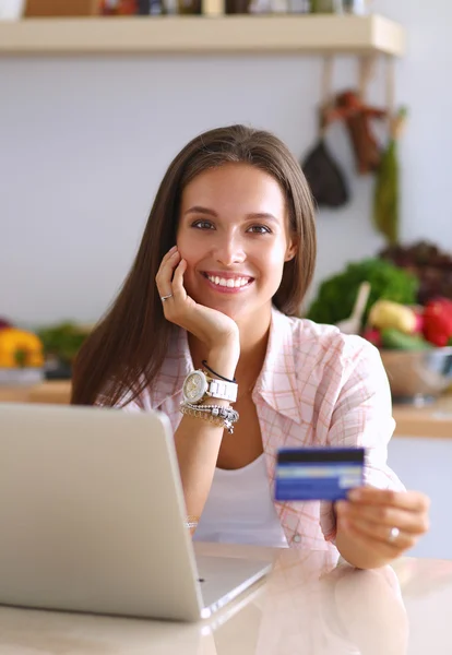 Mulher sorrindo compras on-line usando tablet e cartão de crédito na cozinha — Fotografia de Stock