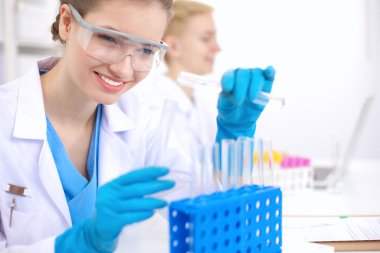 Kadın araştırmacı, beyaz arka planda izole edilmiş ilaç şişeleri ve mataralarla çevrili.