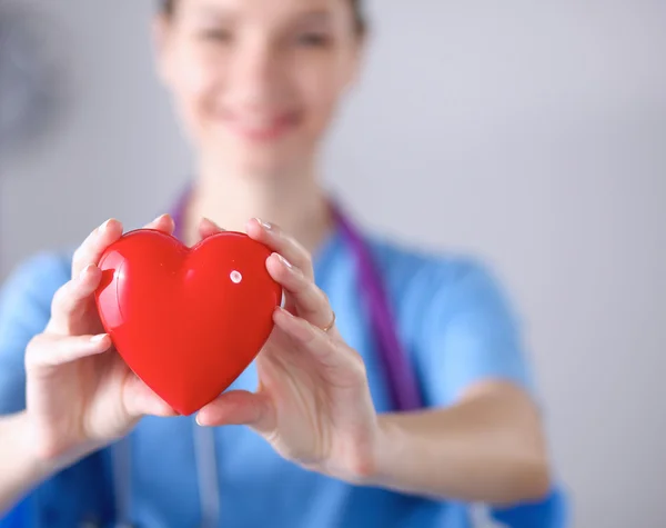 Mujer joven médico sosteniendo un corazón rojo, de pie sobre fondo gris — Foto de Stock