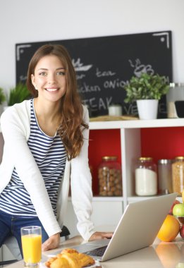 Dizüstü bilgisayar kullanarak ve mutfakta oturmuş çekici genç kadın