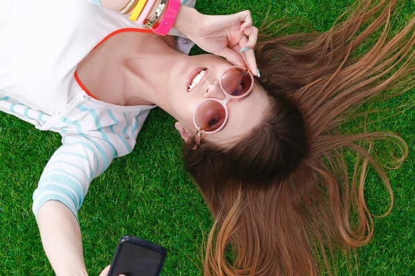 Bela jovem mulher fazendo selfie por seu telefone enquanto deitado na grama verde — Fotografia de Stock