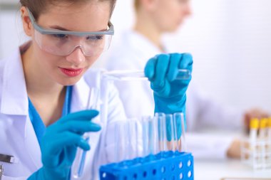 Kadın araştırmacı, beyaz arka planda izole edilmiş ilaç şişeleri ve mataralarla çevrili.