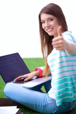 Laptoplu genç bir kadın yeşil çimlerde oturuyor.