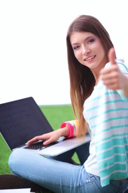 Laptoplu genç bir kadın yeşil çimlerde oturuyor.