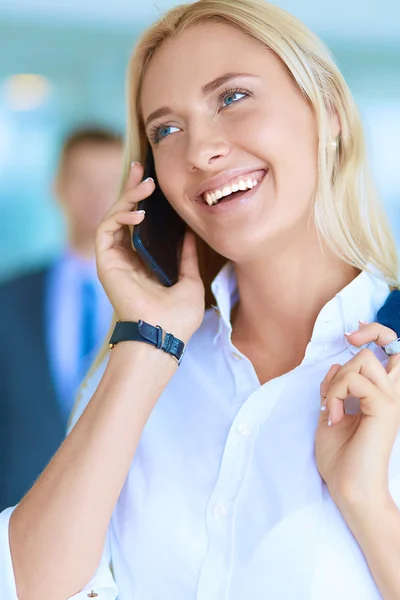 Affärskvinna står mot kontorsfönster talar på mobiltelefon — Stockfoto