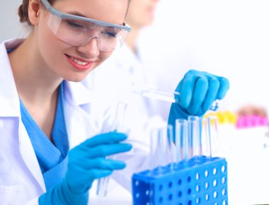 Kadın araştırmacı, beyaz arka planda izole edilmiş ilaç şişeleri ve mataralarla çevrili.