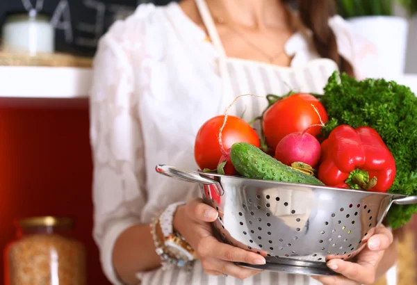 Young woman holding vegetables standing in kitchen — Stock Photo, Image