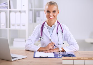 Güzel, genç, gülümseyen bayan doktor masada oturuyor ve yazıyor..