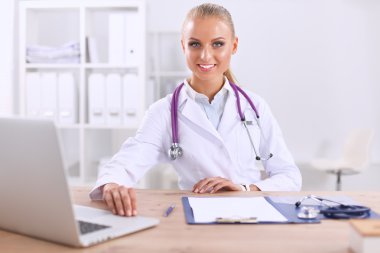 Güzel, genç, gülümseyen bayan doktor masada oturuyor ve yazıyor..