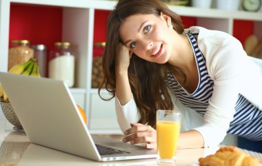 Dizüstü bilgisayar kullanarak ve mutfakta oturmuş çekici genç kadın