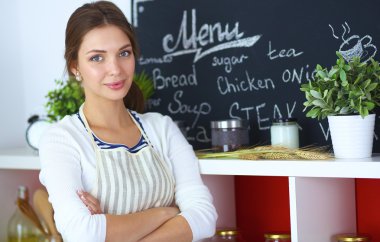 Genç bir kadın mutfakta duruyor.